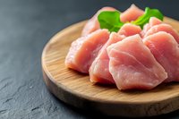 Fresh raw pork meat chunks on wooden cutting board with basil leaves, dark stone background with copy space. Healthy protein food preparation.