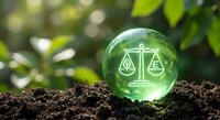 Green crystal sphere with scales of justice symbol resting on rich soil against blurred natural foliage background representing environmental law and sustainability.