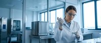 Young male scientist in white lab coat and glasses conducting research in modern laboratory, holding test tube with sample for analysis and experimentation.