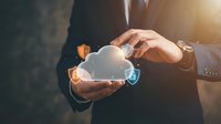 Businessman in formal suit holding glowing cloud icon with connected security shield symbols, representing cloud computing, data protection, and network technology solutions.