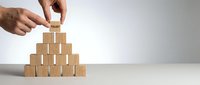 Businessman hands building wooden block pyramid on white desk representing growth strategy and leadership development in corporate environment.