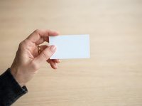 Male hand holding blank white business card against wooden background for branding and corporate identity mockup designs.