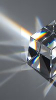 Crystal prism refracting sunlight into rainbow spectrum on white surface creating colorful light dispersion and optical physics demonstration.