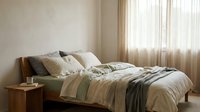 Cozy bedroom interior with unmade bed featuring striped bedding in neutral tones, wooden nightstand, and sheer curtains filtering natural light for home decor and lifestyle design projects.