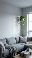 Minimalist living room corner with gray upholstered sectional sofa, hanging pothos plant in natural light from window, neutral interior design with books and cozy textiles.