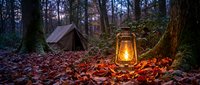 Vintage oil lantern glowing warmly beside camping tent in autumn forest at dusk, creating cozy outdoor adventure atmosphere with fallen leaves and tall trees.
