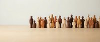 Diverse wooden figurines in various skin tones standing in a row on neutral background, representing community, diversity, inclusion, teamwork and human connection for business concepts.