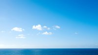 Serene seascape with calm blue ocean waters meeting clear sky with scattered white clouds, suitable for travel and nature backgrounds.