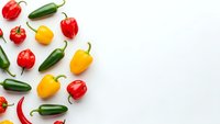 Fresh colorful bell peppers and chili peppers scattered on white background with copy space for healthy cooking and spice ingredient concepts.