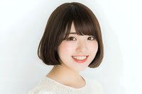 Young Asian woman with short bob hairstyle and bangs smiling warmly at camera against white background, wearing cream-colored knit sweater. Natural makeup and friendly expression.