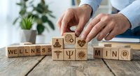 Professional arranging wooden blocks spelling wellness and mind with health symbols on desk for mental wellbeing and healthcare concepts.