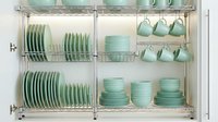 Organized kitchen cabinet with mint green dishes, plates, and mugs on chrome wire shelving, showcasing modern storage and home organization.