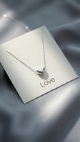 Silver heart pendant necklace on a love gift card, placed on soft gray satin fabric, romantic jewelry concept for Valentine's Day.