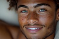 Close up portrait of young mixed race man with freckles, curly hair and bright blue eyes smiling genuinely at camera against blurred background.