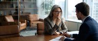 Professional businesswoman with glasses conducting interview or meeting with male colleague in modern office conference room for corporate recruitment.