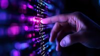 Finger pointing at digital code display with purple and blue bokeh lights, programming interface background showing binary data and software development.
