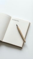 Open gratitude journal with "Grateful for:" prompt and wooden fountain pen on white surface for mindfulness and wellness practices.