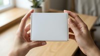 Female hands holding white product box on wooden table with natural window light, suitable for packaging mockups and e-commerce presentations.
