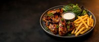 Grilled chicken wings with herbs and spices served with golden french fries and creamy dipping sauce on dark plate for restaurant menu and food delivery.