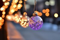 Purple Christmas ornament hanging with warm bokeh lights creating festive holiday atmosphere for seasonal decorations and greeting cards.