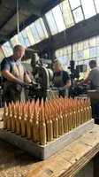 Ammunition manufacturing facility with workers producing brass cartridges and copper bullets in industrial workshop setting for defense industry.