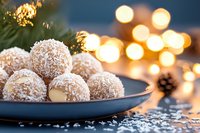 Homemade coconut snowball truffles on blue plate with festive bokeh lights and pine cone in background, winter holiday dessert photography.