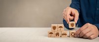 Businessman hand arranging wooden blocks with insurance icons including health, home, car and life protection symbols on white desk for risk management.