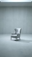 Gray upholstered wingback chair in minimalist concrete interior space. Modern furniture design for home decor, interior styling, and contemporary living room concepts.