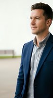 Professional male in navy blazer and light blue shirt standing outdoors, looking to side with confident expression. Suitable for corporate, business, and professional website use.