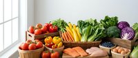 Fresh organic vegetables, fruits, salmon, chicken and eggs arranged on kitchen counter for healthy meal preparation and cooking.