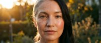 Middle-aged Asian woman with natural makeup and gentle expression in warm golden hour sunlight outdoors for lifestyle and wellness content.