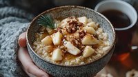 Creamy oatmeal topped with caramelized pears, walnuts, and honey in gray ceramic bowl, served with hot tea. Cozy winter breakfast setting with knitted texture.