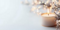 Glowing candle with soft bokeh lights and winter branches creates serene holiday atmosphere on white background, copy space for seasonal greetings.