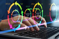 Software development lifecycle concept with colorful circular arrows showing deploy, test, feedback loop stages over laptop keyboard and hands typing.