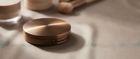 Luxury golden cosmetic compact powder case with mirror on beige surface with soft shadows. Premium makeup packaging design for beauty and skincare brands.