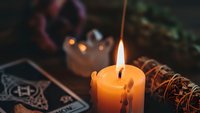 Mystical candle flame illuminates tarot cards and sage bundle creating atmospheric fortune telling scene for spiritual practices and divination rituals.