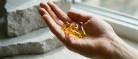 Close-up of hand holding golden supplement capsule near window with natural light, wellness and health concept for nutritional products and vitamin marketing.