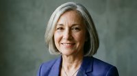 Senior woman with gray hair and warm smile wearing blue blazer against neutral background for corporate and professional use.