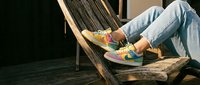 Person relaxing in wooden deck chair wearing colorful sneakers and light blue jeans on sunny day for leisure lifestyle content.