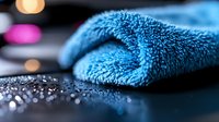 Folded blue microfiber towel on wet surface with water droplets and blurred bokeh lights in background, suitable for spa, cleaning, and household product marketing.