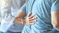 Medical professional in white coat examining male patient's back, focusing on spine alignment during physical therapy session. Professional healthcare consultation.