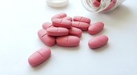 Pink oval tablets scattered from white medicine bottle on clean surface for pharmaceutical and healthcare concepts.
