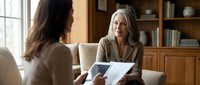 Professional mature Caucasian businesswoman consultant meeting with female client in modern office discussing documents and paperwork consultation.