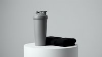 Protein shaker bottle with black towel on white podium, fitness and gym equipment for workout nutrition and sports hydration needs.