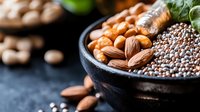 Mixed nuts and seeds in black ceramic bowl on dark background with almonds, chia seeds and cashews. Healthy protein-rich superfood ingredients for cooking.