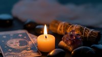 Mystical fortune telling setup with burning candle, tarot cards, crystals and sage bundle creating atmospheric spiritual divination scene for meditation practices.
