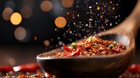 Red hot chili pepper flakes and spices falling on wooden spoon with blurred bokeh lights background, dramatic food photography for restaurant menu design.