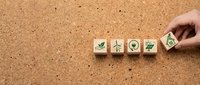 Hand placing wooden cubes with green eco symbols on cork surface representing sustainable business practices and environmental responsibility.