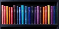 Colorful hardcover books arranged in rainbow spectrum order on dark wooden shelf, creating vibrant visual display for education, literature and library concepts.