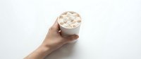 Hand holding a white paper cup of hot chocolate topped with marshmallows on a white background, isolated for design use.